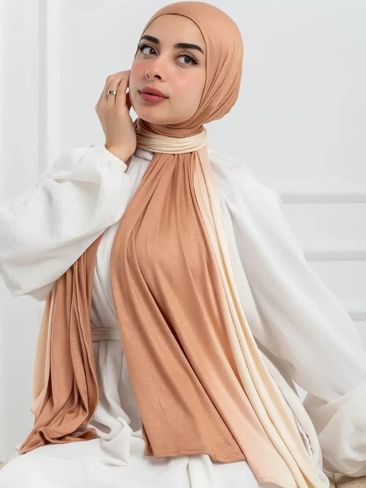 Una mujer vistiendo un pañuelo hijab de algodón con degradado rosa empolvado y blanco sobre ropa blanca.