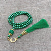 Grüne Perlenrosary-Armband mit goldenen Akzenten und einem grünen Quasten auf grauem Stoff.
