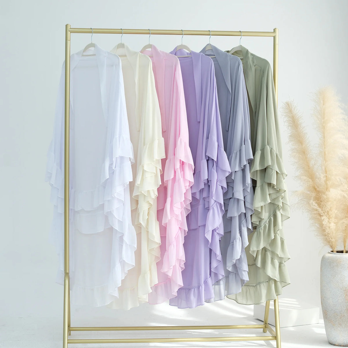 A display of ruffled two-layer chiffon hijabs in pastel shades hanging on a gold hanger rack.