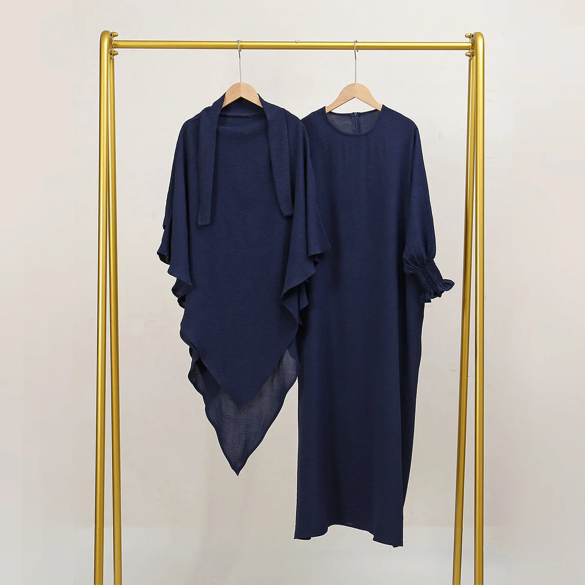 A navy blue elegant two-piece abaya and khimar set displayed on a gold hanger against a light background.