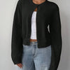 Une femme portant un pull cardigan noir tricoté sur un jean délavé clair.