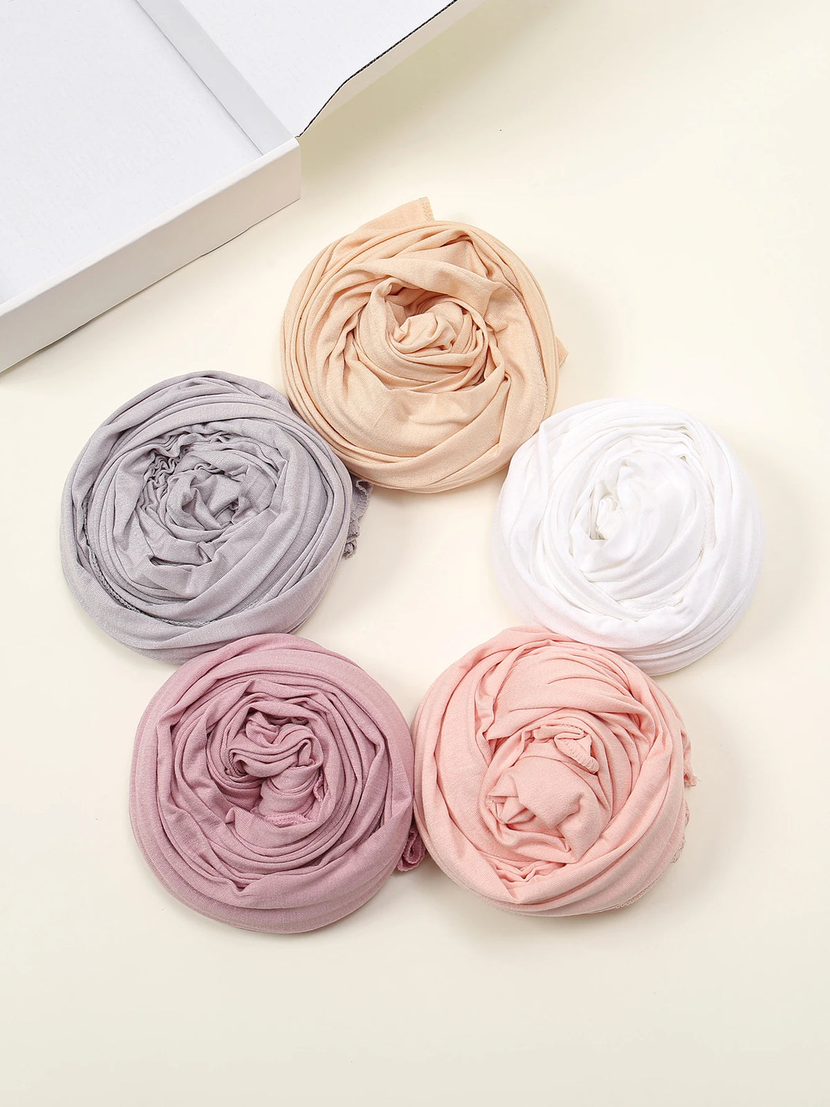 Ein Set von fünf einfarbigen Jersey-Hijab-Schals in Beige, Grau, Weiß und Pink sind in einem Kreis angeordnet.