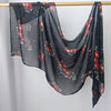Durchsichtiger, dunkelgrauer Hijab-Schal mit Blumenmuster hängt an einem Holzstab.