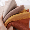 A hand is holding several rolled ribbed jersey hijab scarves in shades of beige, brown, and gold.