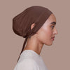 Une femme portant un bonnet de hijab intérieur en corde marron, vue de profil sur fond neutre.