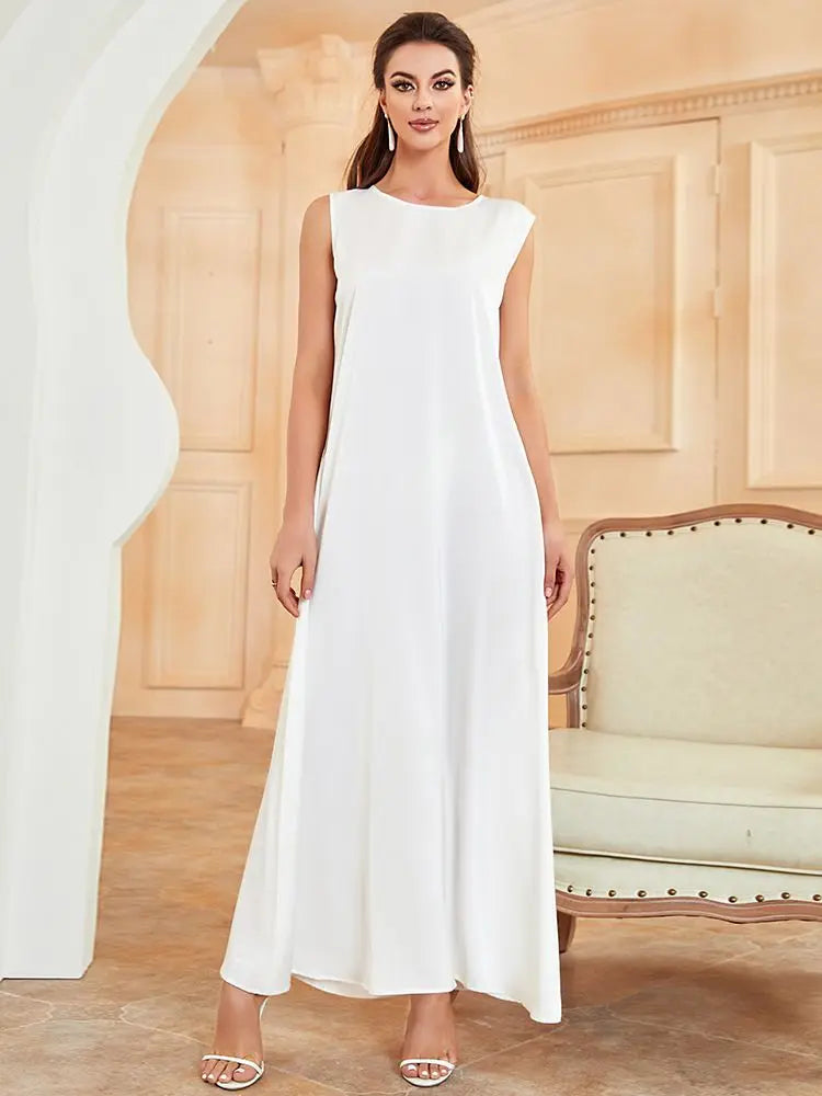 A woman wearing a white flowing modest abaya dress in a light beige room.