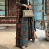Une femme portant un long trench à motifs sur une robe noire et tenant un sac beige dans un décor moderne.
