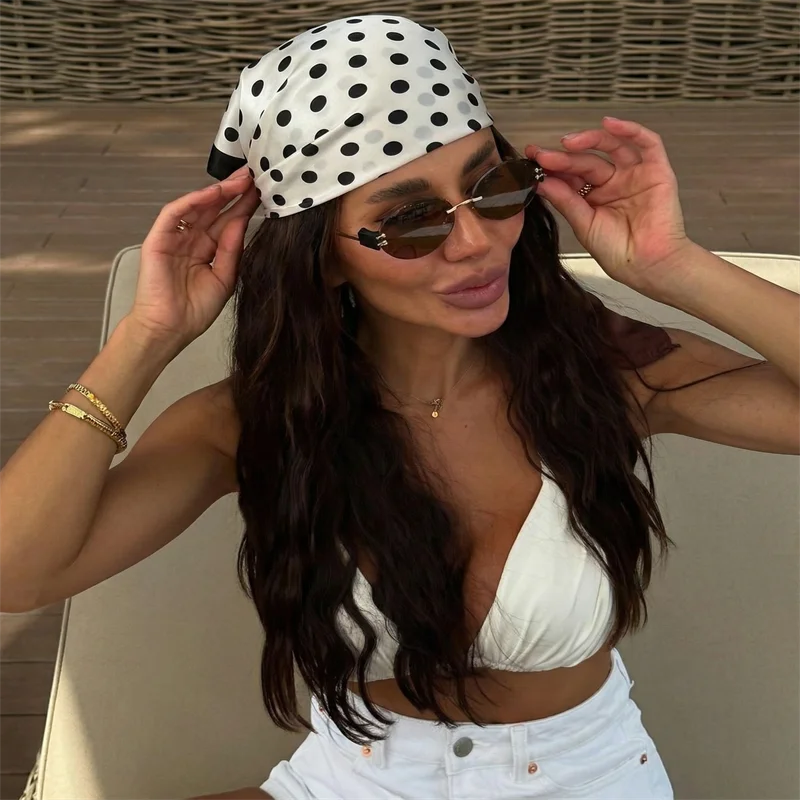 A woman wearing a white polka dot cap, sunglasses, and a white crop top and jeans.