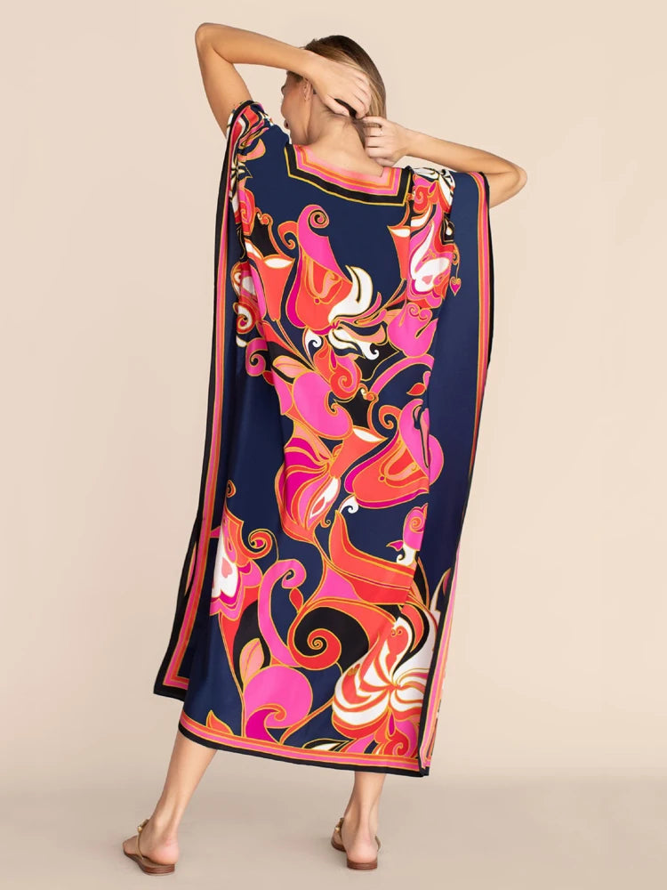 Una mujer modela un vibrante caftán de playa con estampado floral abstracto en rosa, naranja y azul marino.