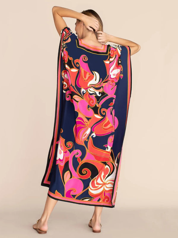 A woman models a vibrant, flowing kaftan beach cover-up dress featuring an abstract floral print in pink, orange, and navy bl