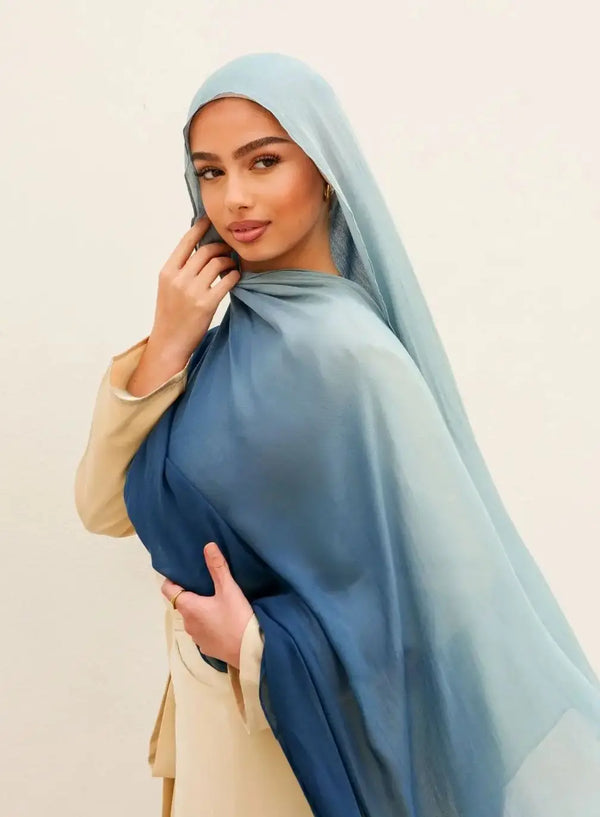 A woman wearing a flowing ombre gradient blue hijab scarf and a cream top.