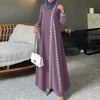 Eine Frau trägt ein langes lila Abaya-Kleid mit weißer Spitze und trägt eine weiße Tasche.