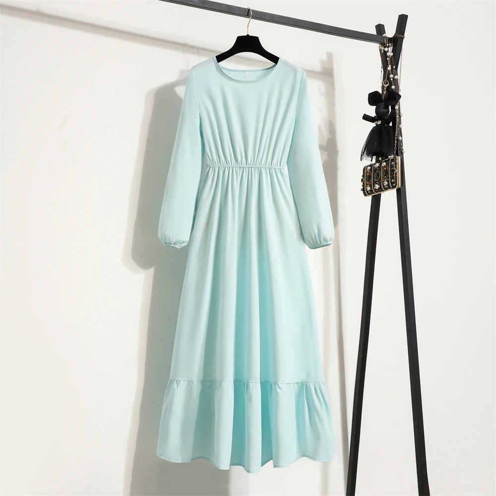 Mintblauer Boho-Blumenmuster-Maxikleid an einem schwarzen Haken vor einer weißen Wand.