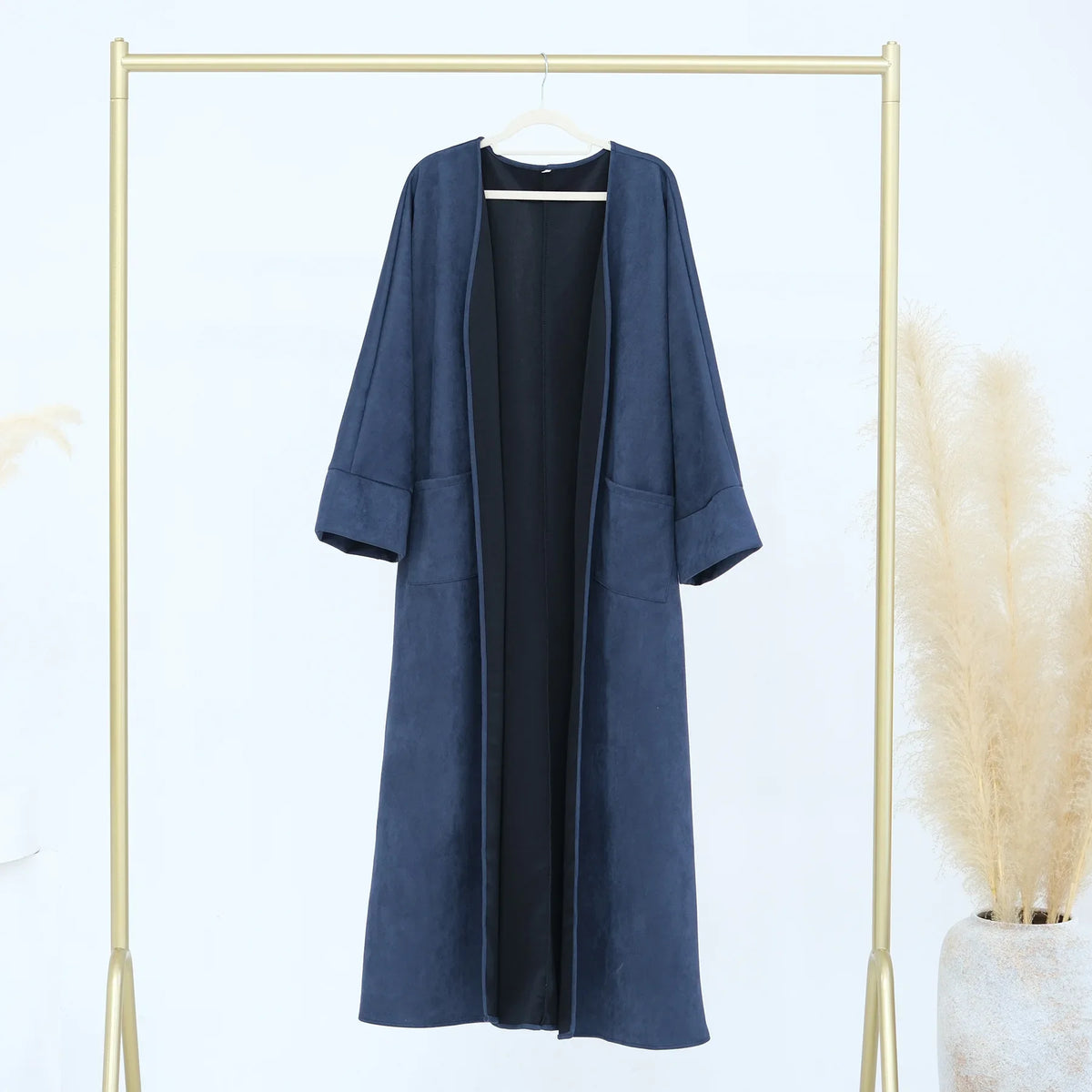 A navy blue elegant women's abaya trench coat hanging on a gold-toned hanger against a white background.