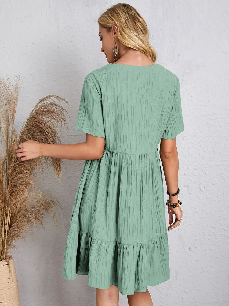 Eine Frau trägt ein elegantes, einfarbiges mintgrünes A-Linien-Minikleid mit kurzen Ärmeln und gerafftem Saum.
