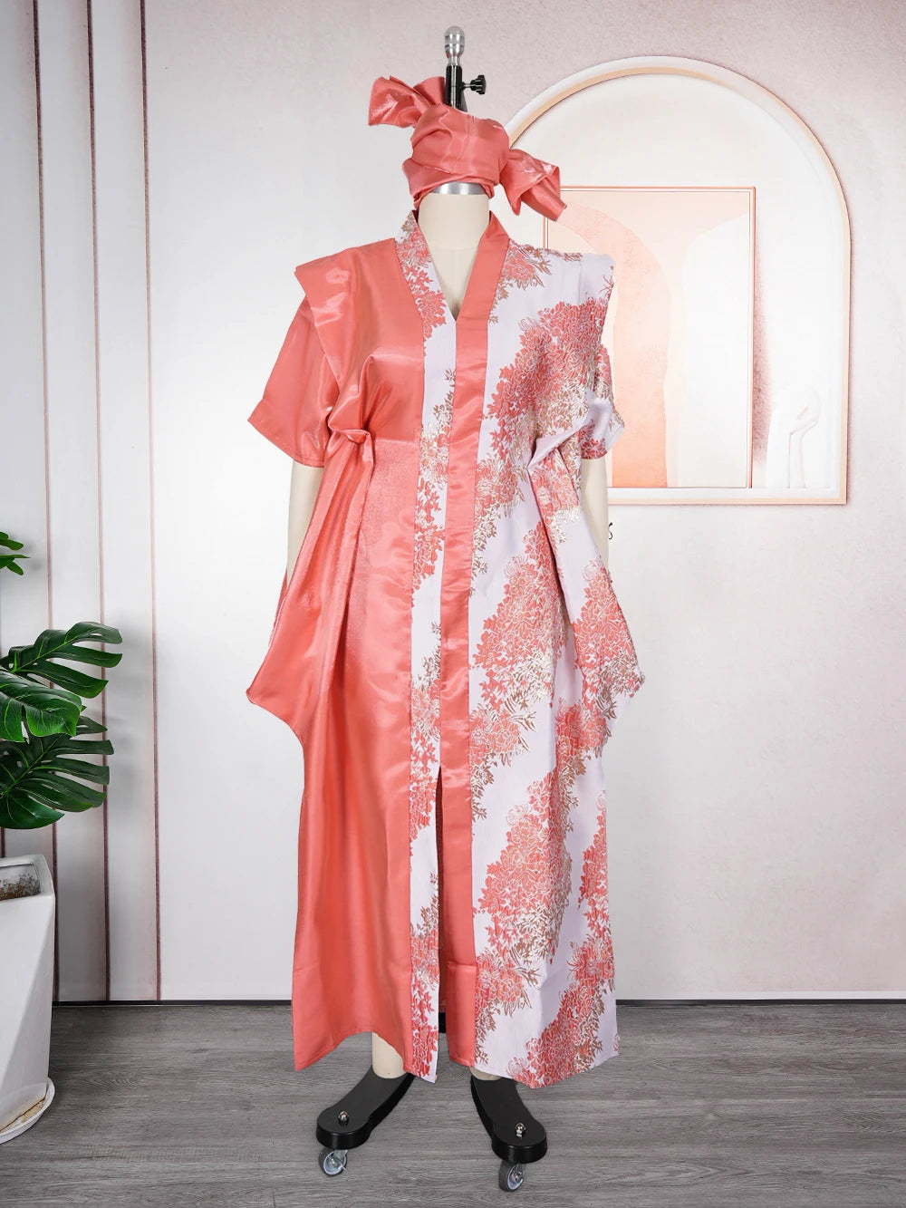 A woman wearing an elegant flowing pink kaftan with white tatting detail, displayed on a mannequin.