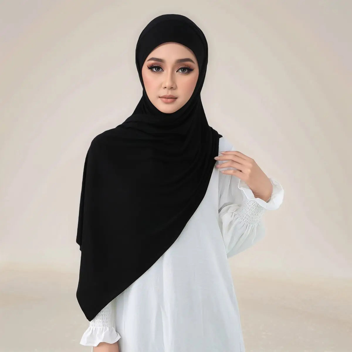 Eine Frau trägt einen schwarzen Instant-Hijab und ein weißes Oberteil, das die Elastizität des Modal-Jersey-Stoffes zeigt.