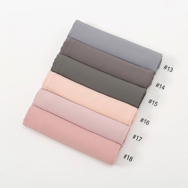 Eine Stapel von achtzehn Premium-Chiffon-Hijab-Schals in verschiedenen Grau- und Rosatönen.