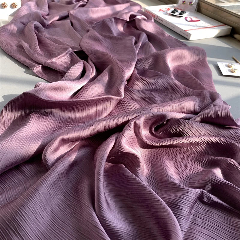 Violettes, gerafftes Satin-Chiffon-Hijabgewebe auf einer hellen Oberfläche.