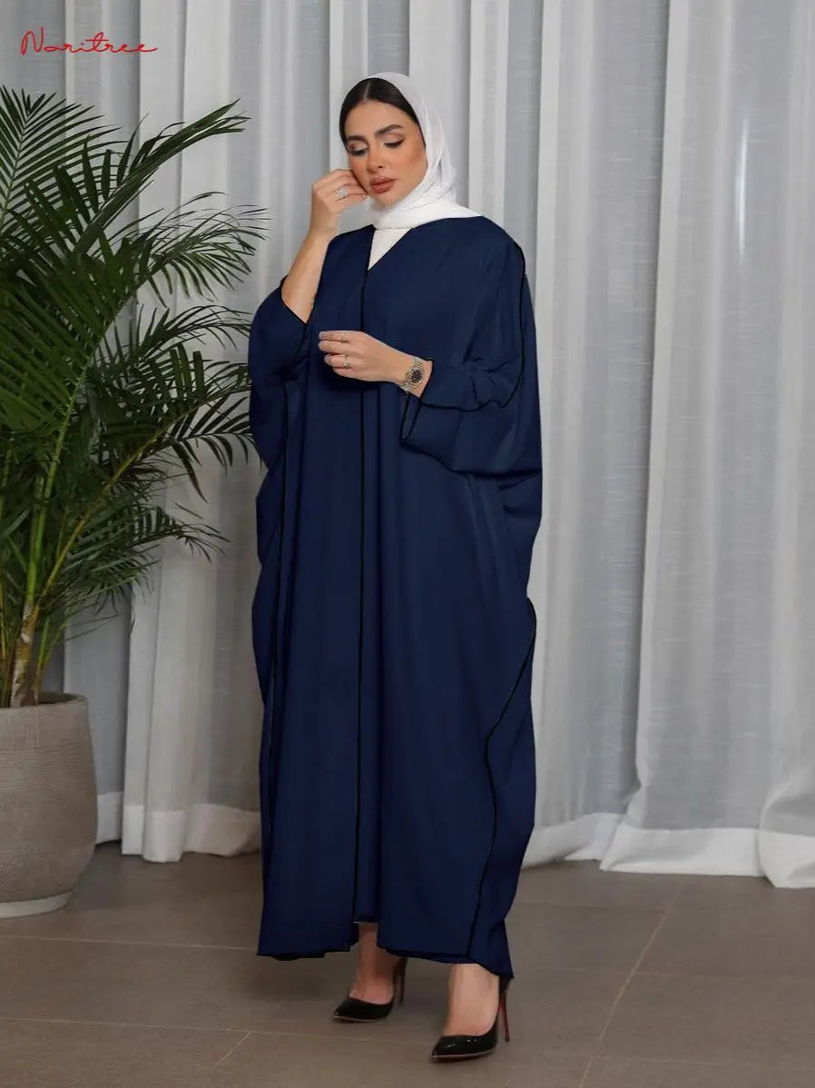 Una mujer vistiendo una abaya azul marino holgada con hijab blanco y tacones negros.