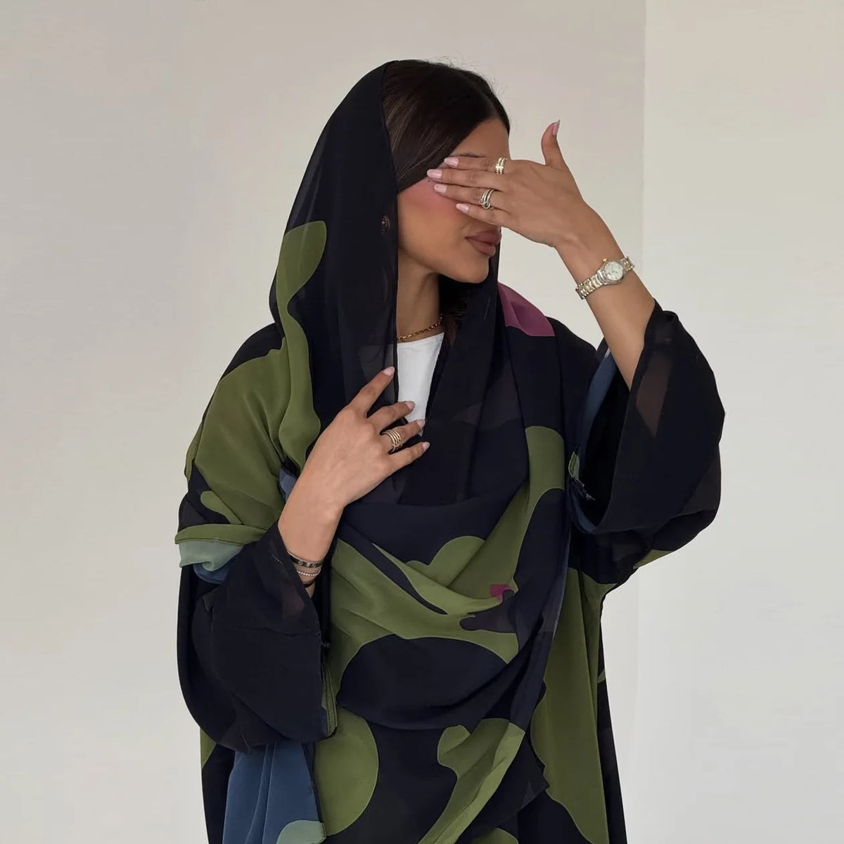 Una mujer vistiendo un conjunto de abaya de gasa estampada en verde oscuro y negro con un hiyab negro transparente.