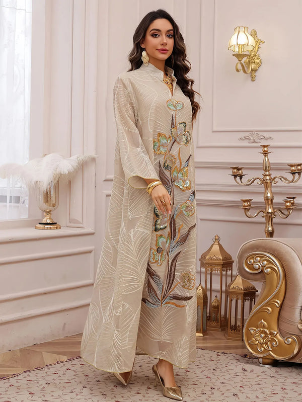 A woman models a beige abaya with gold embroidery and sequins in a light setting.