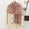 Abrigo beige colgado en una percha con un chal de bordado paisley multicolor sobre él.