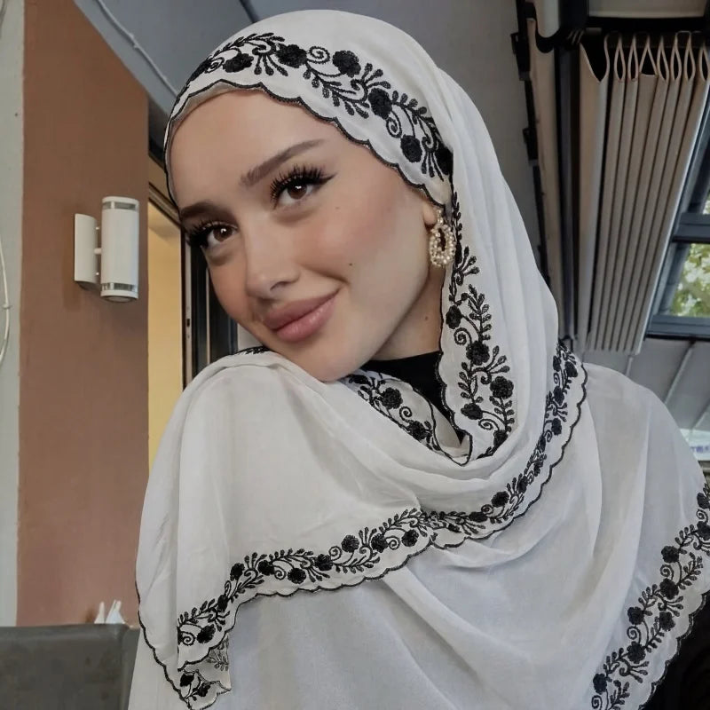 Une femme portant un foulard chiffon blanc avec broderie florale noire et un bord en dentelle à cils.