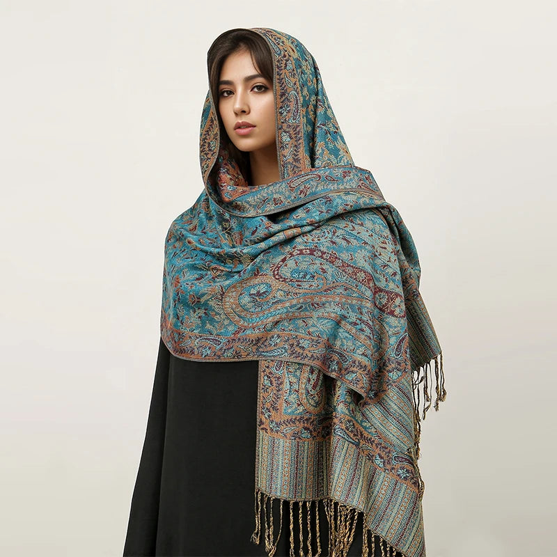 Una mujer modela un pañuelo pashmina de lujo con estampado azul verdoso sobre su cabeza y hombros.