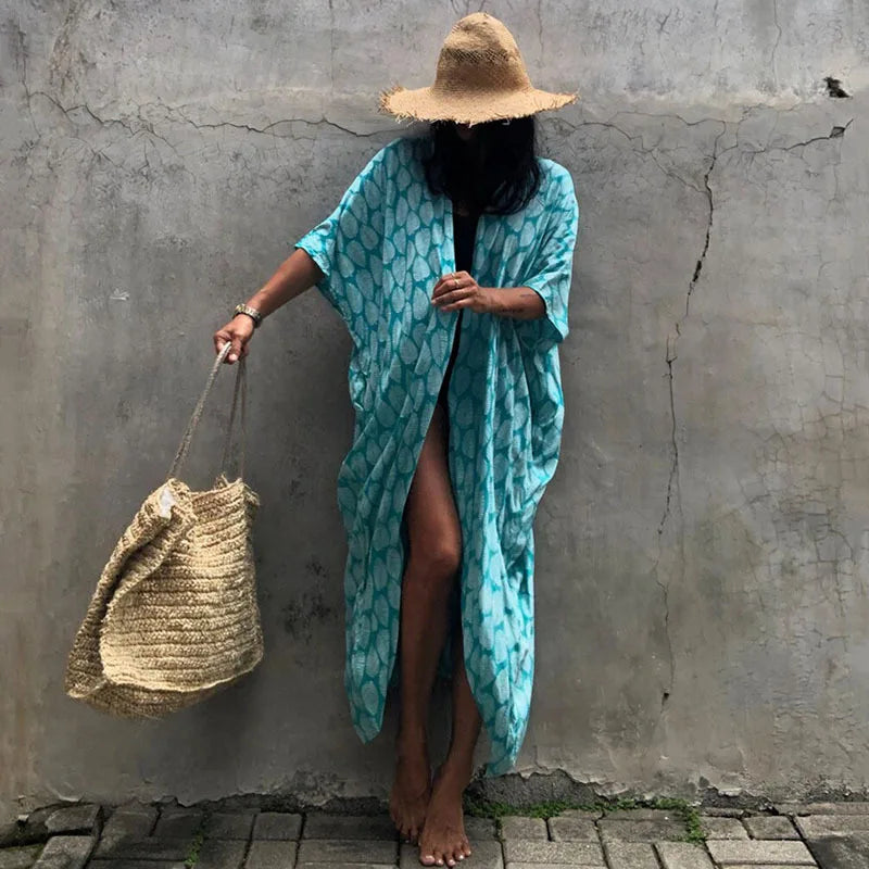 Eine Person in einem hellblauen gemusterten Kimono-Überkleid und einem Strohhut vor einer grauen Wand.