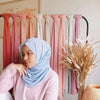 Eine Frau mit einem hellblauen Chiffon-Hijab-Schal wird auf einem Regal mit verschiedenfarbigen Schals präsentiert.
