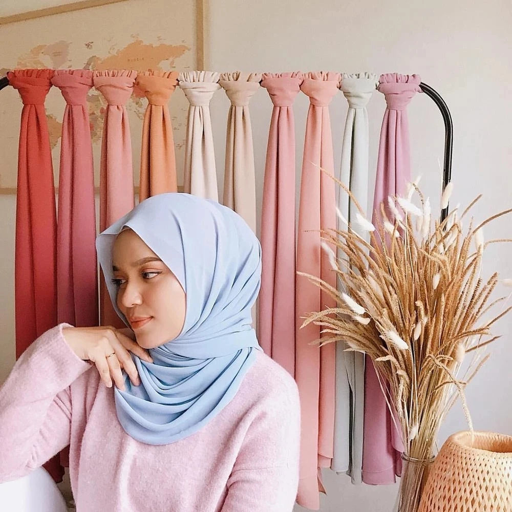 Eine Frau mit einem hellblauen Chiffon-Hijab-Schal wird auf einem Regal mit verschiedenfarbigen Schals präsentiert.