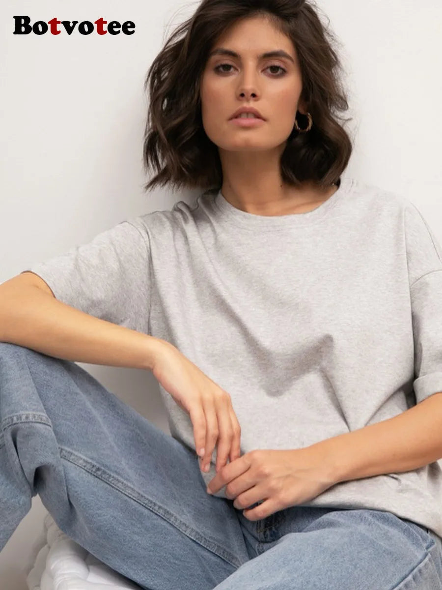 Una mujer vistiendo una camiseta básica de algodón gris claro oversize y jeans azules, sentada.