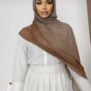 Eine Frau trägt einen braunen Ramanda Bamboo Modal Rayon-Schal-Hijab über einem weißen Oberteil und einem plissierten Rock.