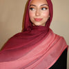 Eine Frau trägt einen pinken Hijabschal mit einem kastanienbraunen Ton vor neutralem Hintergrund.