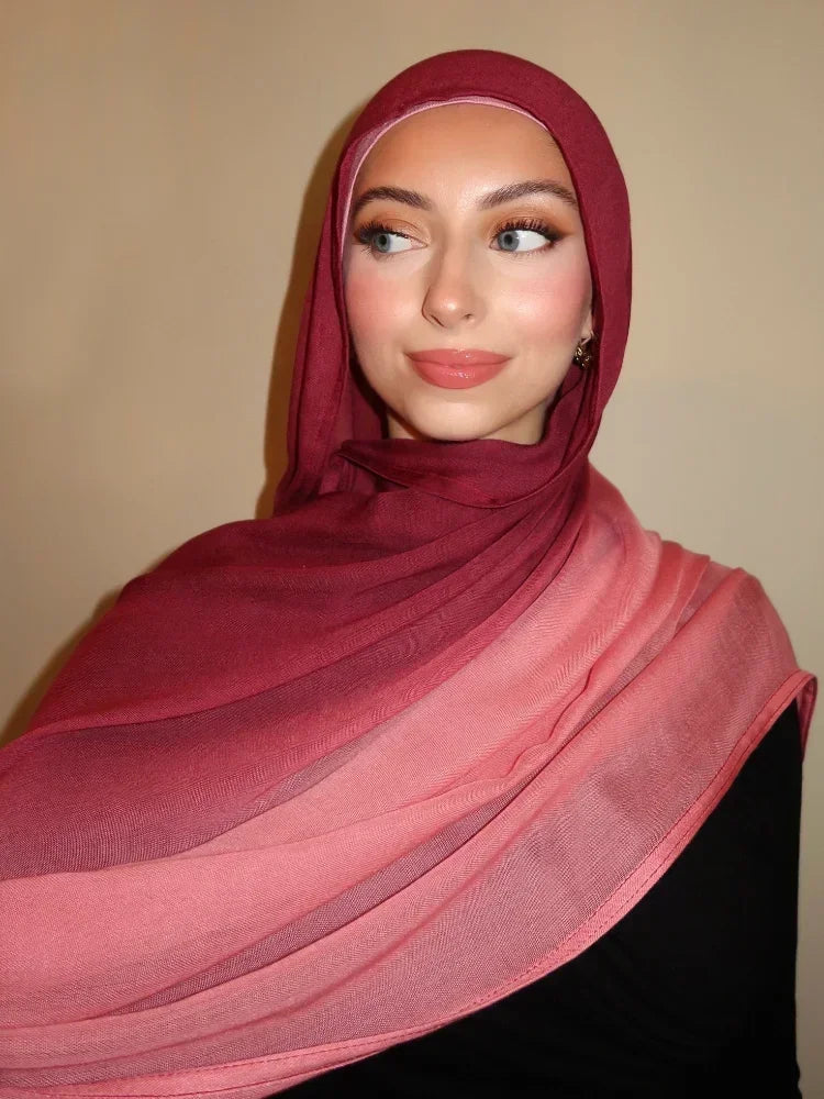 Eine Frau trägt einen pinken Hijabschal mit einem kastanienbraunen Ton vor neutralem Hintergrund.