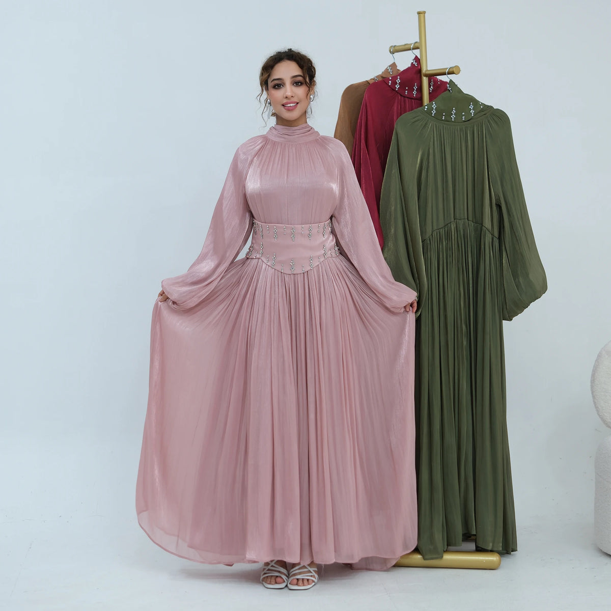 Une femme modélise une abaya en mousseline rose fluide avec une ceinture ornée et une tenue assortie verte.