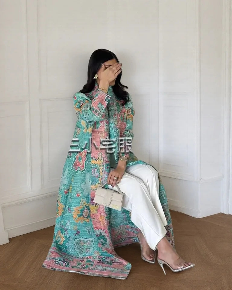 Una mujer vistiendo un cárdigan abaya plisado largo y fluido de color turquesa y rosa con pantalones blancos.