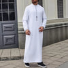 Ein Mann trägt einen weiß bestickten Jubba Kaftan mit schwarzen Akzenten, steht im Freien.