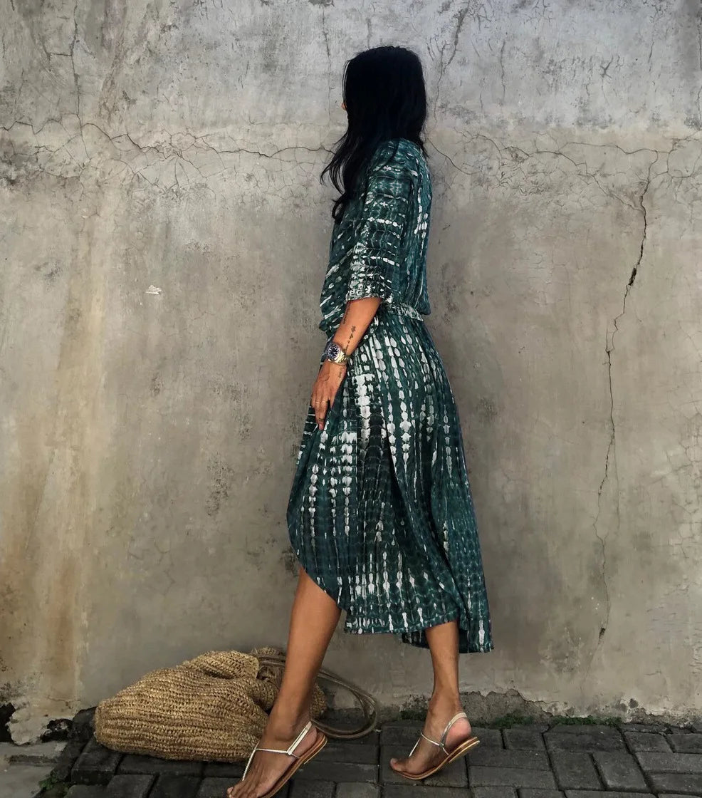 Eine Frau in einem dunkelgrünen gemusterten Sommer-Strandkimono-Überkleid steht vor einer strukturierten grauen Wand.