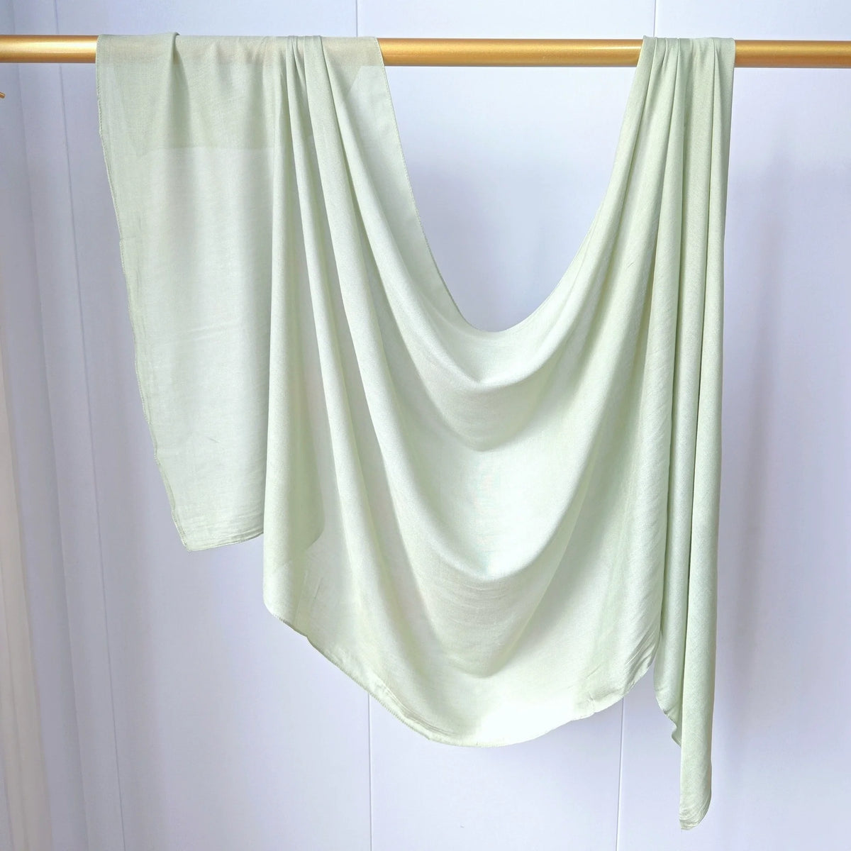 Foulard modal vert sauge clair drapé sur un cintre en bois.