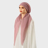 Une femme portant un carré de hijab et un foulard assortis de couleur rose poussiéreux.
