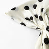 Nahaufnahme eines satinierten Stoffes mit schwarzen Polkadottern in cremefarbener, gefaltet, um den Fall zu zeigen.