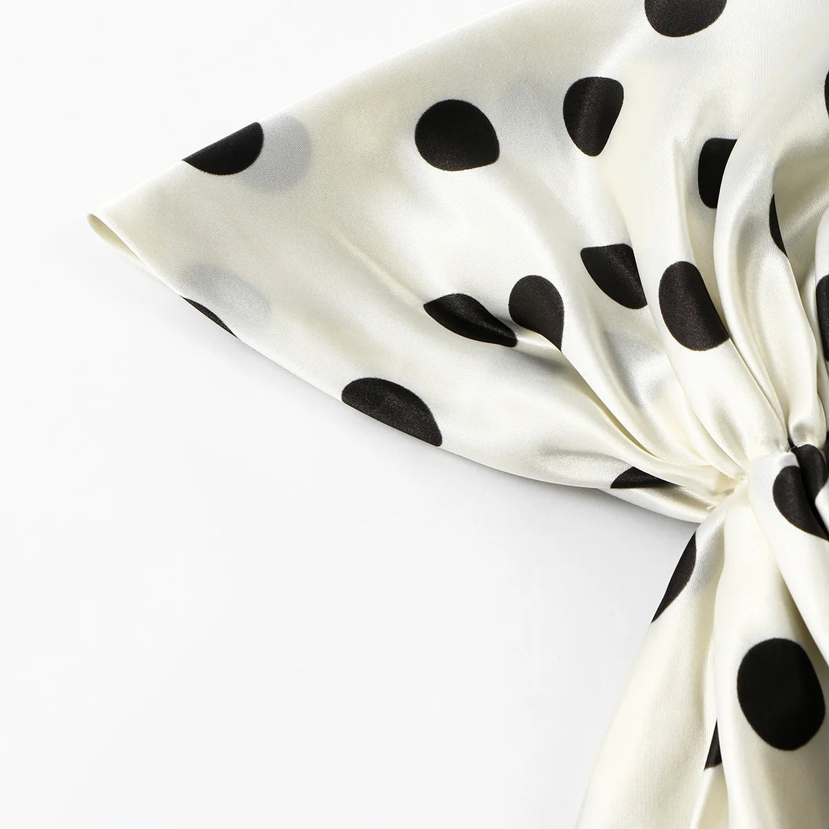 Nahaufnahme eines satinierten Stoffes mit schwarzen Polkadottern in cremefarbener, gefaltet, um den Fall zu zeigen.