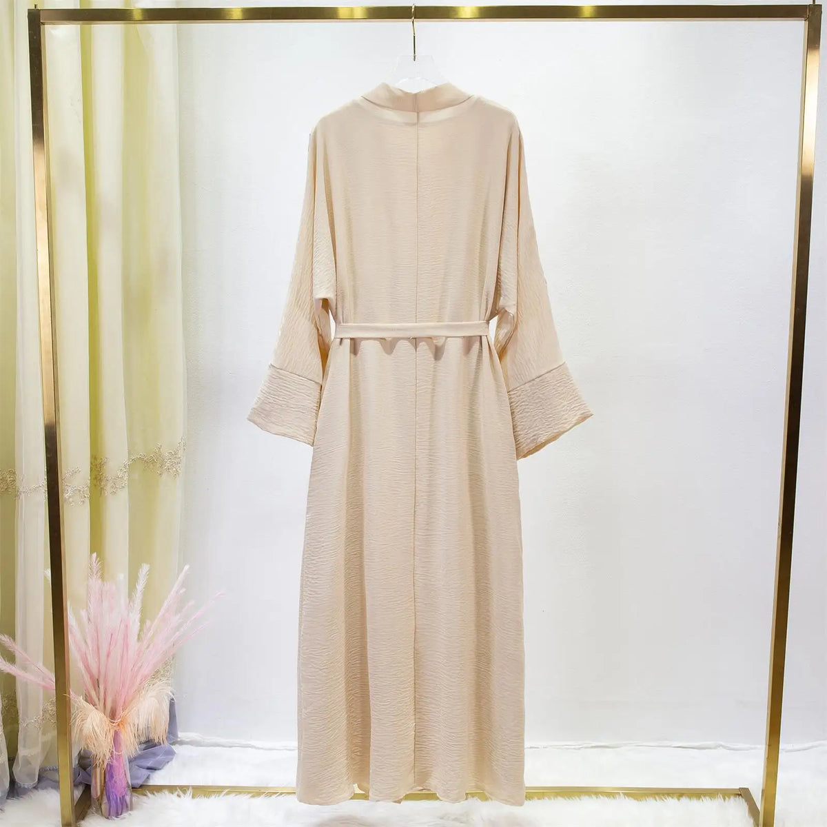 Un conjunto de jilbab beige de dos piezas para mujeres, exhibido en percha contra un fondo blanco.