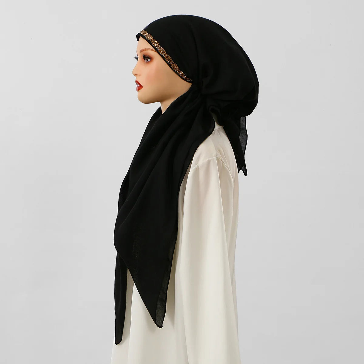 Una mujer vistiendo un hiyab negro con una diadema elástica de diamante dorado y una blusa color crema.