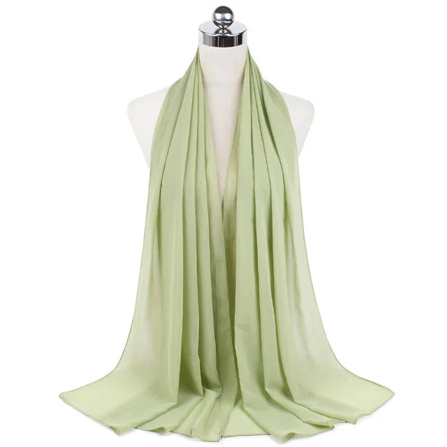 A light sage green chiffon hijab scarf draped around a mannequin's neck.