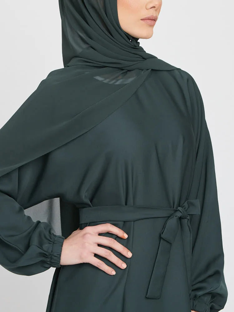Eine Frau trägt eine dunkeltürkise marokkanische Kaftan-Abaya mit langen Ärmeln und einem drapierten Kopftuch.