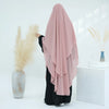 Eine Frau mit pinker, zweilagiger Chiffon-Niqab und schwarzer Kleidung steht neben einer Vase mit getrockneten beigen Blumen.