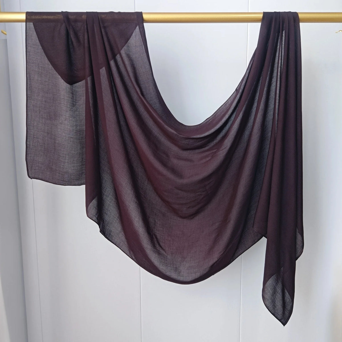 Écharpe hijab de couleur prune foncée drapée sur un cintre en bois.